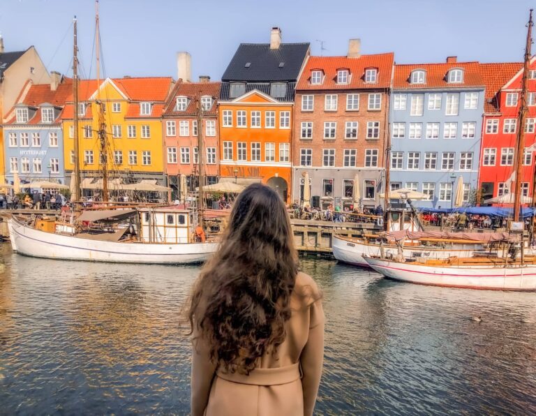 Woman in beige coat from behind, city centre of Copenhagen with colorful houses near the sea