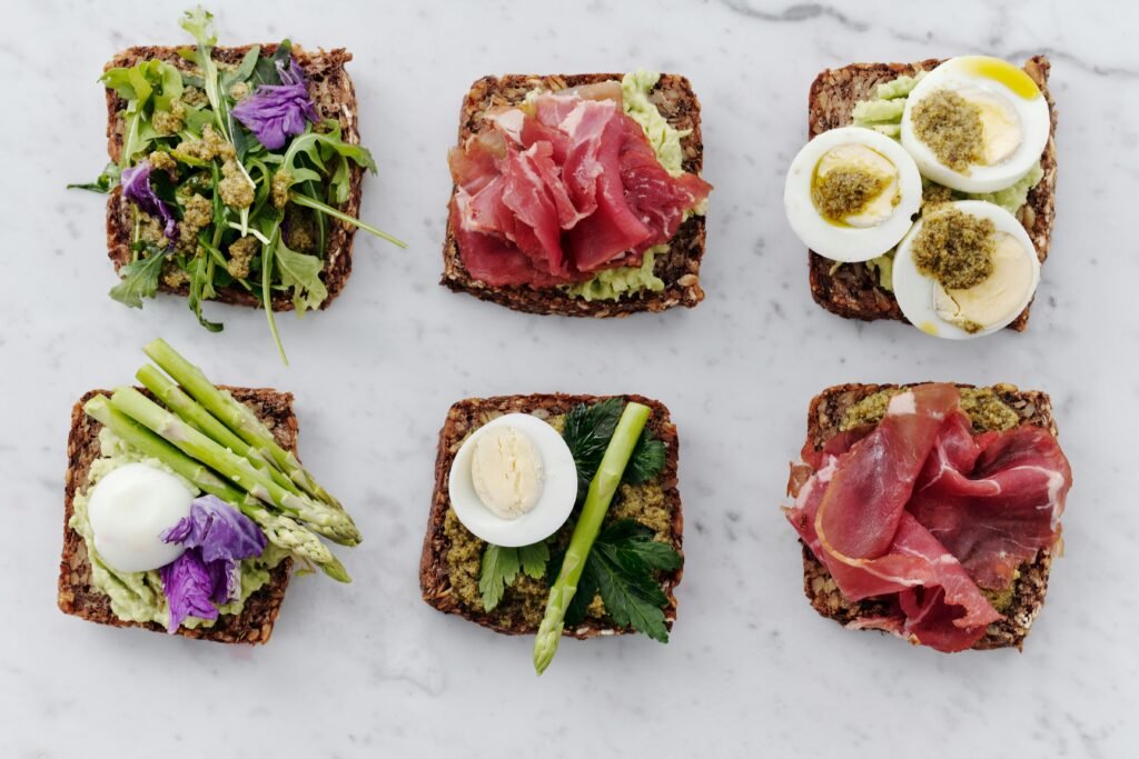 Danish meals - Traditional Danish Food Guide: Famous Meals from Smørrebrød to Flæskesteg - Career Denmark Top view of six gourmet sandwiches featuring artisanal ingredients like avocado, asparagus, and cured meats.