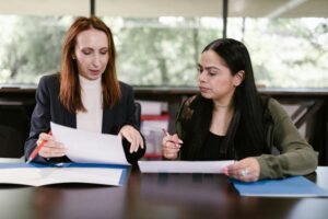 Two woman discussing papers behind table